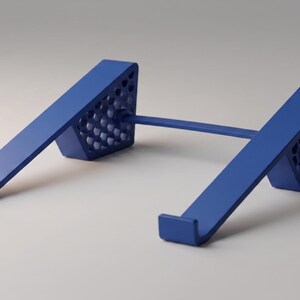 May include: A blue tablet stand with a minimalist design. The stand has two angled supports connected by a horizontal bar. The supports have a perforated pattern on the sides and a small lip to hold a tablet. The stand is made of a solid material.