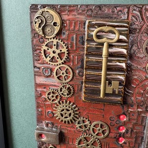 May include: A steampunk-themed artwork featuring a textured, reddish-brown background with embedded metal gears and a brass key. The design incorporates various sizes of gears, a small clock face, and a rectangular element with a key.