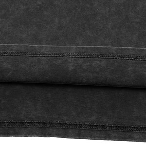 May include: A charcoal black fabric with a washed, faded appearance featuring a horizontal hemline. The material displays a visible ribbed texture and a double-stitched seam running horizontally across the lower section of the garment.