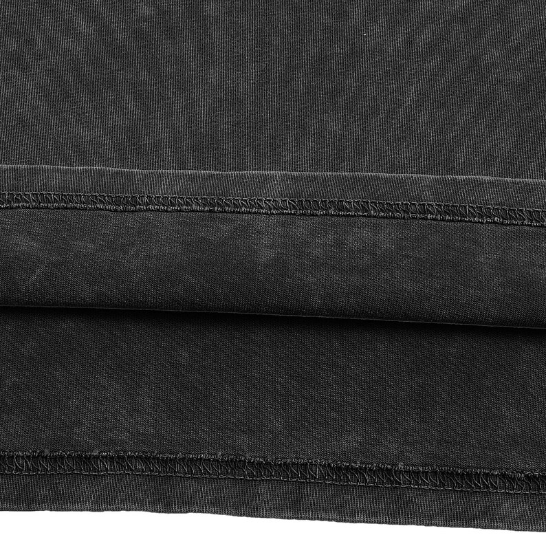 May include: A charcoal black fabric with a washed, faded appearance featuring a horizontal hemline. The material displays a visible ribbed texture and a double-stitched seam running horizontally across the lower section of the garment.