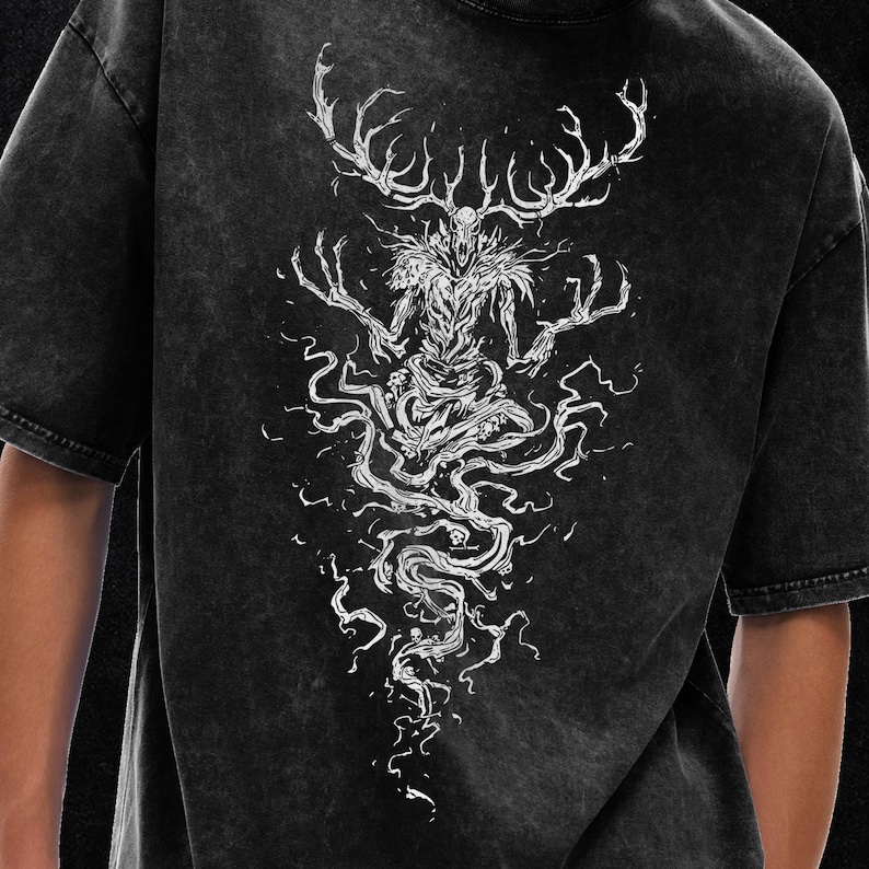 May include: A black acid-wash t-shirt featuring a large white graphic print on the back. The design depicts a skeletal, antlered creature with long, clawed fingers, surrounded by swirling, smoke-like patterns and small skull motifs.