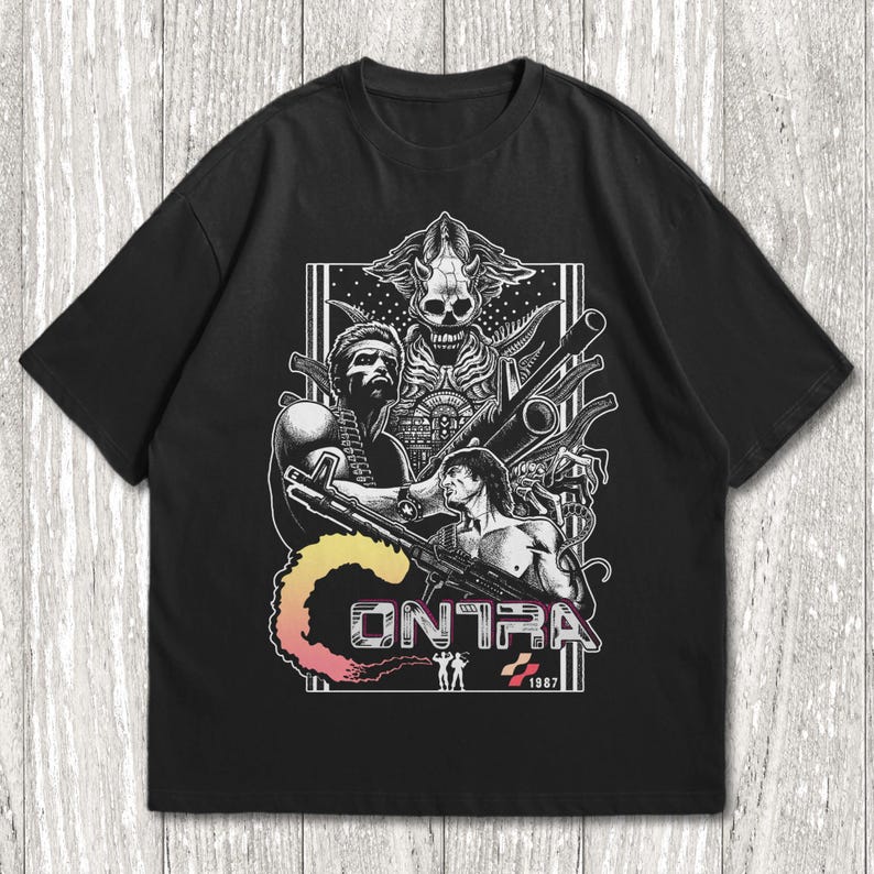 K&ouml;nnte beinhalten: Ein schwarzes Kurzarm-T-Shirt mit einem detaillierten wei&szlig;en Grafikdruck von zwei muskul&ouml;sen Soldaten, die gro&szlig;e Gewehre halten. &Uuml;ber ihnen befindet sich eine totenkopfartige Kreatur. Das Wort CONTRA ist in einem Farbverlauf aufgedruckt.