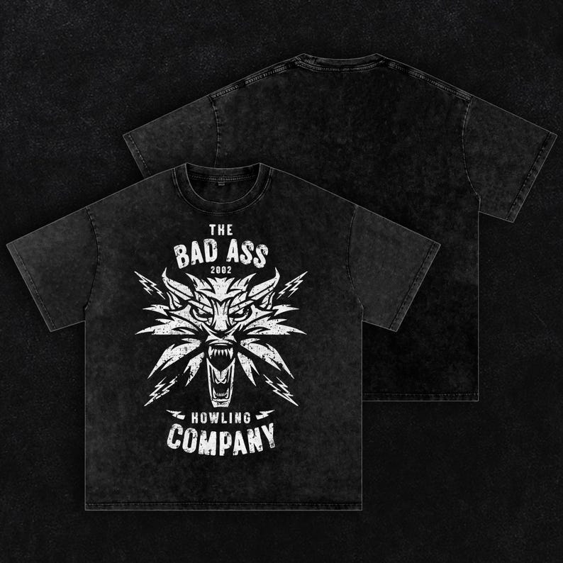 Peut inclure: Un t-shirt noir d&eacute;lav&eacute; &agrave; l'acide avec un motif blanc repr&eacute;sentant une t&ecirc;te de loup stylis&eacute;e et des &eacute;clairs. Le texte indique THE BAD ASS 2002 HOWLING COMPANY. Le motif pr&eacute;sente un aspect vieilli et us&eacute; sur le devant, le dos est uni.