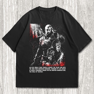 May include: A black short-sleeved t-shirt featuring a graphic illustration of a warrior with a sword. The design includes red accents and text that reads: AN EPIC WORLD TOUR TRAVELS ACROSS THE GLOBE AND INTO THE WAR-TORN NORTHERN KINGDOMS, BRINGING TO LIFE GERALT OF RIVIA'S LEGENDARY SEARCH FOR HIS ADOPTED DAUGHTER CIRI, THE CHILD OF DESTINY.