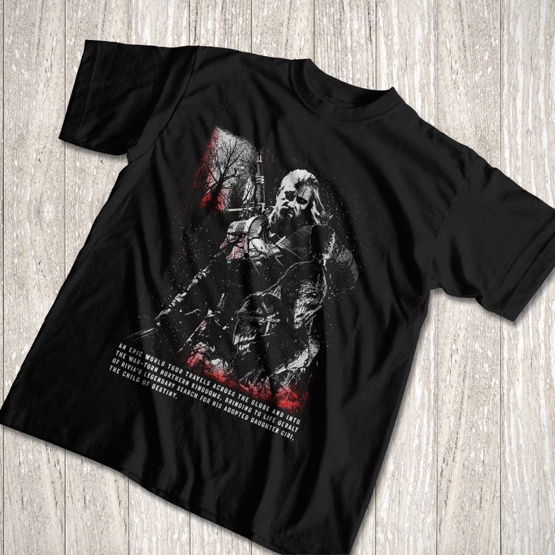 May include: A black short-sleeve t-shirt featuring a graphic illustration of a warrior with a sword. The design includes red and white accents and text that reads: An epic world tour travels across the globe and into the war-torn northern kingdoms.