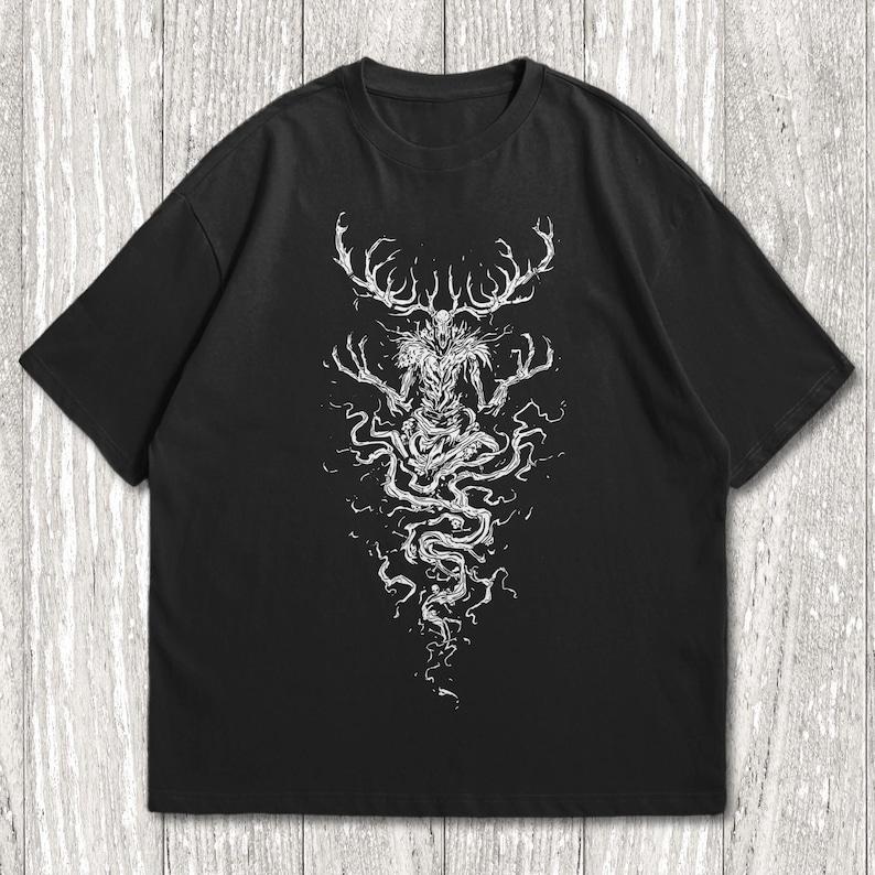 May include: A black short-sleeved t-shirt featuring a white graphic print on the front. The design depicts a skeletal, antlered creature with long, spindly fingers and a flowing, root-like lower body that extends downward in a swirling pattern.