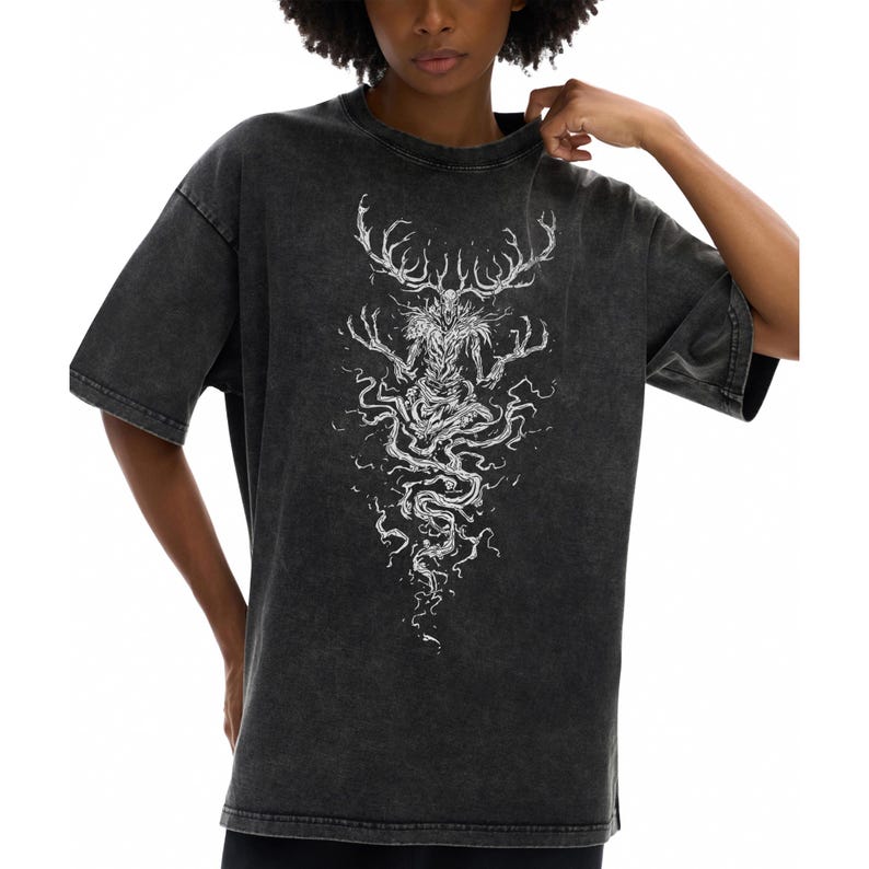 May include: A charcoal gray acid-wash t-shirt featuring a white graphic print of a skeletal, antlered creature with elongated fingers and flowing, root-like tendrils extending downward from its torso, centered on the front of the garment.