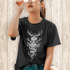 May include: A black short-sleeved t-shirt featuring a white graphic print of a skeletal, antlered creature with long, spindly fingers and a flowing, root-like lower body that extends downward in a detailed, intricate line art style.