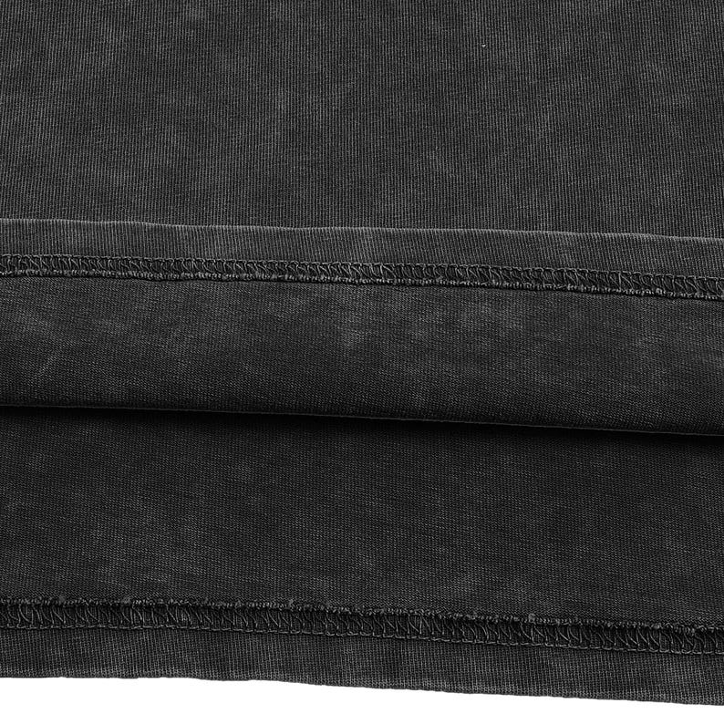 Peut inclure: Un tissu noir anthracite &agrave; l'aspect d&eacute;lav&eacute; et us&eacute; pr&eacute;sentant un ourlet horizontal. Le mat&eacute;riau affiche une texture c&ocirc;tel&eacute;e visible et une couture double surpiq&ucirc;re courant horizontalement sur la partie inf&eacute;rieure du v&ecirc;tement.
