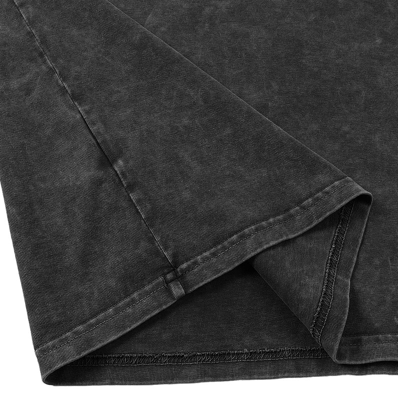 May include: A charcoal gray t-shirt featuring a mineral wash finish. The garment displays a visible side seam and a double-stitched hem along the bottom edge. The fabric has a textured, faded appearance with variations in color intensity throughout.