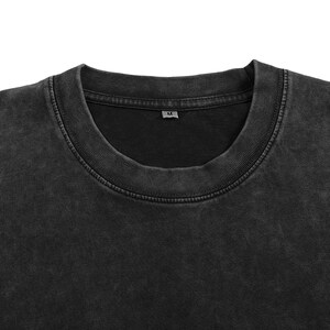 Peut inclure: Un t-shirt &agrave; col rond gris anthracite avec une texture d&eacute;lav&eacute;e et us&eacute;e. Le v&ecirc;tement pr&eacute;sente un col c&ocirc;tel&eacute; et une petite &eacute;tiquette int&eacute;rieure au niveau du cou affichant la lettre M, indiquant la taille. Le tissu a un ton sombre et mat.