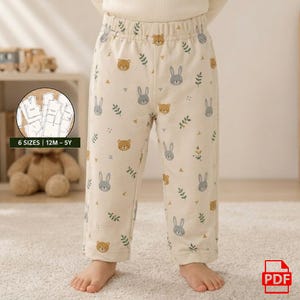 May include: Cream-colored pajama pants with a repeating pattern of gray bunnies, brown bears, and green sprigs. The pants have an elastic waistband and are worn by a child. Text on the image reads "6 SIZES | 12M - 5Y".
