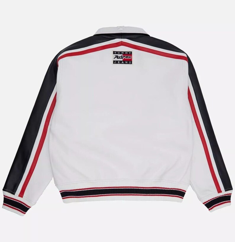 May include: White jacket with black sleeves and red stripes. The jacket has a collar and a ribbed hem with red, white, and black stripes. The back of the jacket features a small logo that says "TOMMY AVIREX JEANS".