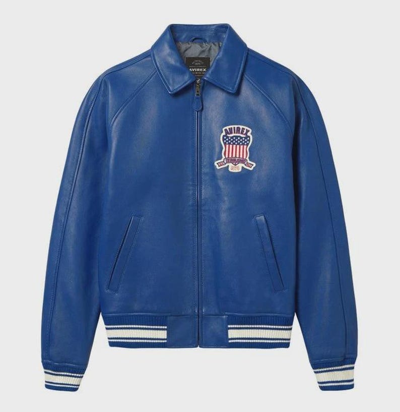 May include: A vibrant blue leather jacket with a classic collar and a zip-up front. Features a patch on the chest with an American flag design and the brand name. The cuffs and hem have white stripes.