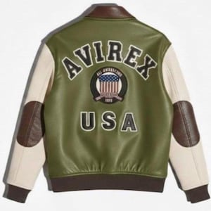 Puede incluir: Chaqueta universitaria Avirex USA verde y crema. La parte trasera de la chaqueta presenta la palabra "AVIREX" sobre un parche circular con un dise&ntilde;o de bandera estadounidense y la palabra "USA" debajo. Detalles en cuero marr&oacute;n en el cuello, codos y pu&ntilde;os.