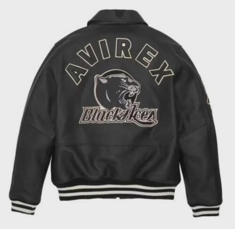 K&ouml;nnte beinhalten: Schwarze Lederjacke mit wei&szlig;-schwarz gestreiften B&uuml;ndchen und Saum. Auf der R&uuml;ckseite steht das Wort "AVIREX" &uuml;ber einer Panther-Grafik und den Worten "Black Aces". Die Jacke hat einen klassischen Kragen.