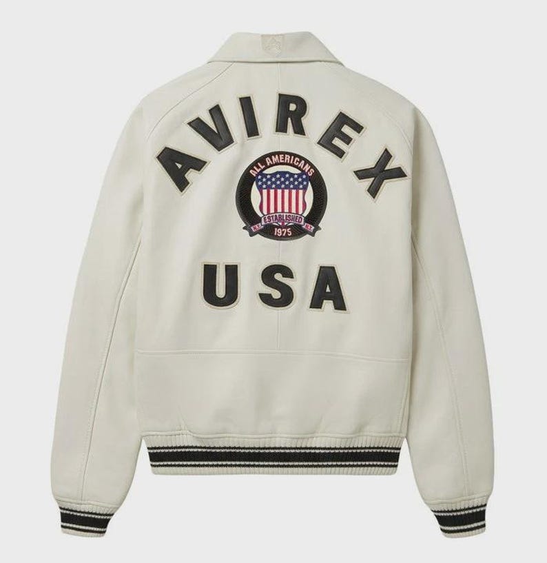 May include: Cream-colored leather jacket with black and white striped cuffs and hem. The back features the word "AVIREX" above a circular patch with the words "ALL AMERICANS ESTABLISHED 1975" and a USA flag design. Below is the word "USA".