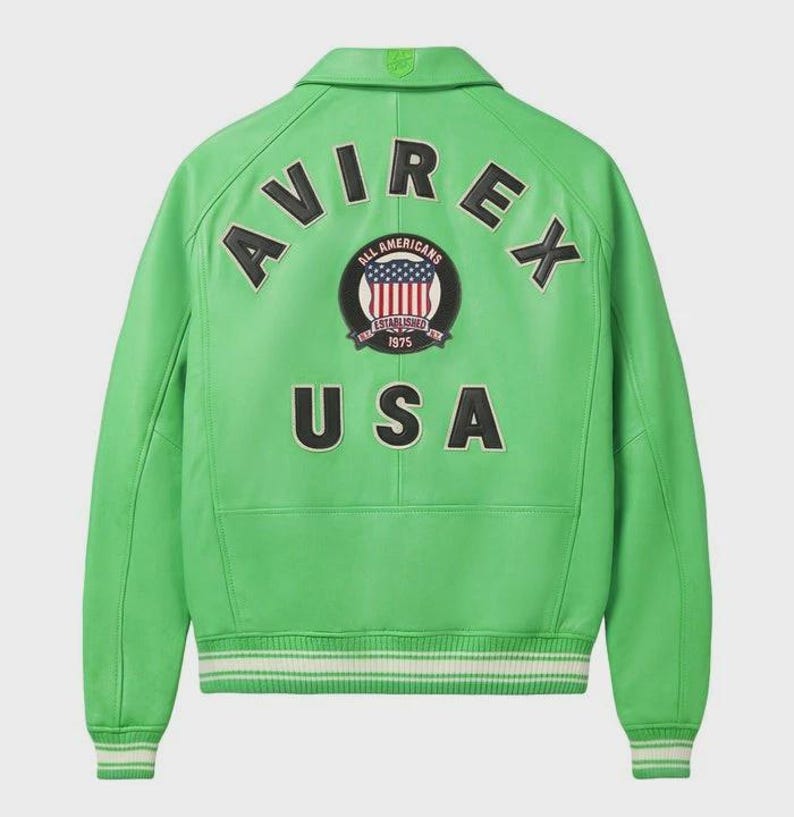 May include: A vibrant green leather jacket featuring the word "AVIREX" across the shoulders, and "USA" below a circular emblem. The emblem displays the American flag and the words "ALL AMERICANS ESTABLISHED 1975". The jacket has a collar and white and green striped cuffs.