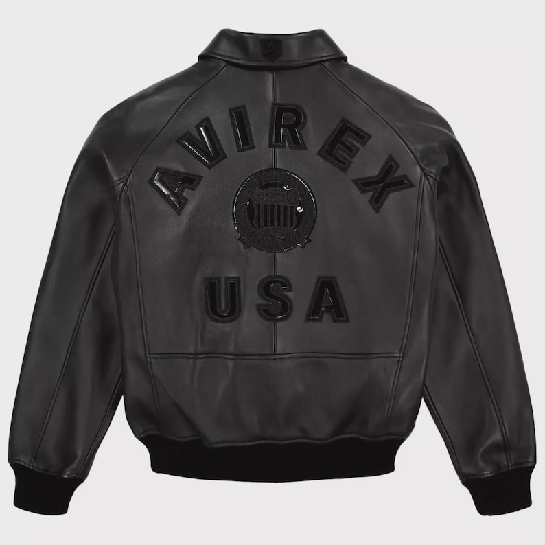 May include: Black leather jacket with the word "AVIREX" arched across the back, above a circular emblem and the word "USA". The jacket has a collar, a black ribbed hem, and cuffs.