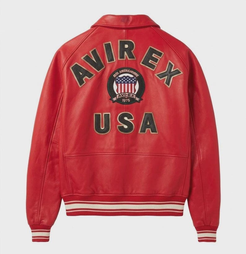 May include: A red leather jacket featuring the word "AVIREX" in black and gold lettering across the shoulders. A circular patch with "AVIREX 1975" and a USA flag design is centered below the lettering. The word "USA" is below the patch.