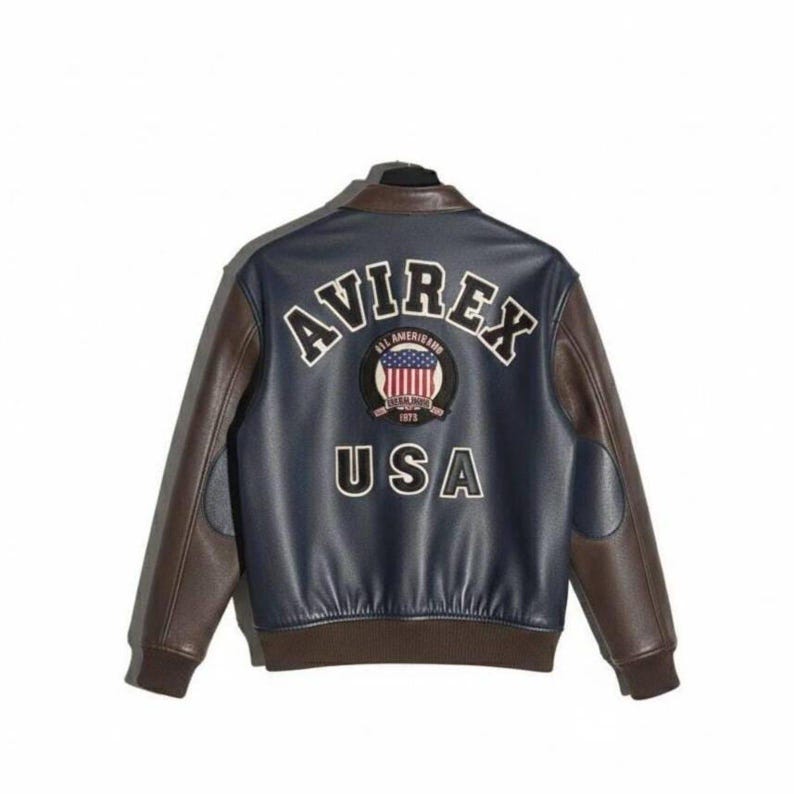 Pu&ograve; includere: Giacca in pelle blu navy e marrone con la scritta "AVIREX" in lettere bianche arcuate sul retro. Sotto, una toppa circolare con la bandiera americana e la scritta "USA".