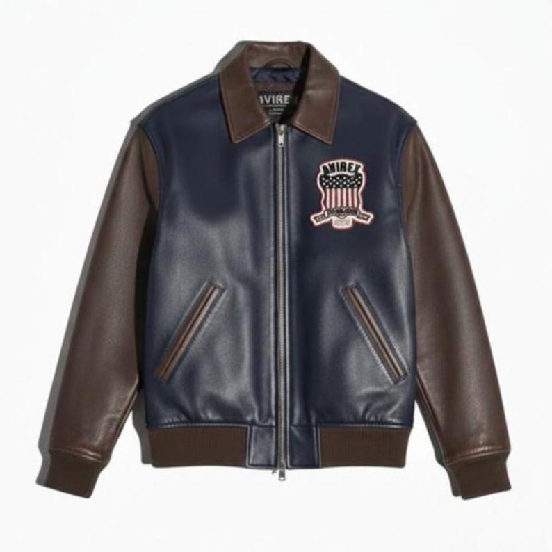 Pu&ograve; includere: Giacca in pelle blu navy e marrone con zip e colletto marrone. La giacca presenta maniche marroni e una toppa sul petto con la scritta "AVIREX" e un disegno della bandiera americana.