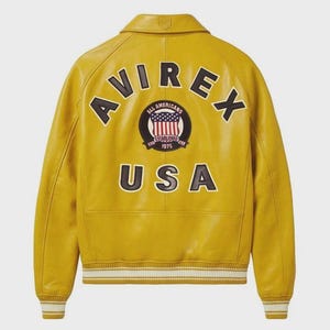 Puede incluir: Chaqueta de cuero amarillo mostaza con la palabra "AVIREX" en letras negras en la espalda. Debajo de la palabra "AVIREX" hay un parche circular con las palabras "ALL AMERICANS" y "ESTABLISHED 1975". La palabra "USA" est&aacute; impresa debajo.