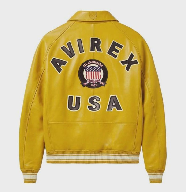 Puede incluir: Chaqueta de cuero amarillo mostaza con la palabra "AVIREX" en letras negras en la espalda. Debajo de la palabra "AVIREX" hay un parche circular con las palabras "ALL AMERICANS" y "ESTABLISHED 1975". La palabra "USA" est&aacute; impresa debajo.