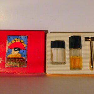 May include: Vintage Lauder grooming set featuring a red box with a framed illustration and a cream-colored tray. The tray holds a small jar, a bottle of liquid, and a gold-colored razor. The Lauder box has a picture of a person wearing a red hat and sunglasses.