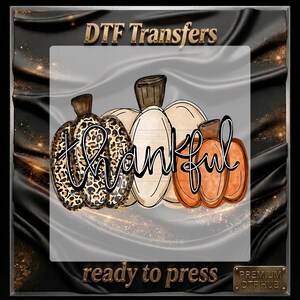 May include: A DTF transfer sheet featuring three pumpkins with the word thankful written in black script across them. The left pumpkin has a leopard print pattern, the centre is cream, and the right is orange. The text DTF Transfers and ready to press is visible.