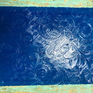 May include: A blue sheet of embossed paper with a white floral pattern. The paper has a textured surface and a glossy finish.