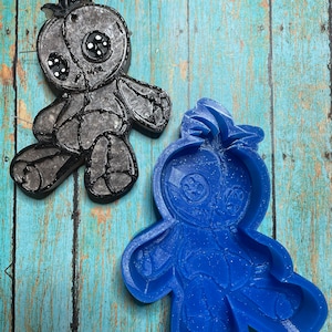 May include: A blue silicone mold of a rag doll with stitched details. The mold is on a blue wooden surface.