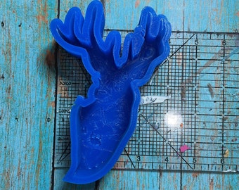 May include: Blue silicone mold of a deer head with antlers. The mold is on a white gridded surface.
