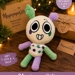 May include: A plush toy with a round cream-colored head, large black eyes, and a stitched smile. It has green and purple ears, arms, and legs, and a white shirt with purple and green polka dots. The text "MagicpopsGifts" is visible.