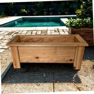 May include: A rectangular wooden planter box featuring a natural light brown wood grain finish, a flat top rim, and four sturdy corner legs. The planter has a hollow center and is constructed from horizontal planks with visible knots.