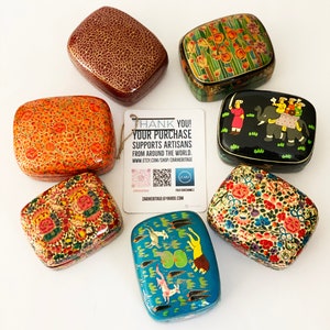 Puede incluir: Una colección de cajas decorativas hechas a mano con diseños intrincados. Las cajas presentan varios patrones, incluyendo motivos florales, animales y abstractos, en una gama de colores. El texto en la etiqueta dice: "THANK YOU! YOUR PURCHASE SUPPORTS ARTISANS FROM AROUND THE WORLD."