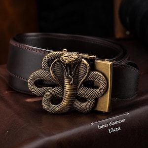 Op de afbeelding: Een bruine leren riem met een cobra-vormige gesp van messing. De gesp heeft ingewikkelde details en een vintage afwerking. De binnendiameter van de gesp is 13 cm.