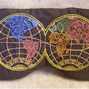 May include: A dark brown sleep mask with two embroidered world map designs. The maps feature continents in blue, pink, green, and orange, outlined in gold thread. The mask is designed to block out light for better sleep.