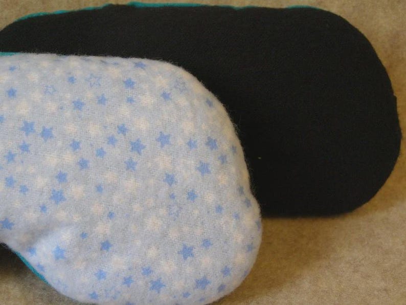 May include: Two eye masks. One is light blue with white and blue stars. The other is black. The edges of the light blue mask are trimmed with teal fabric. The masks are designed to block out light.