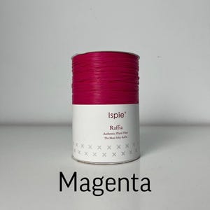 以下が含まれることがあります： Ispieブランドのマゼンタ色のラフィアの円筒形スプール。ラベルには「Ispie」「Raffia」「Authentic Plant Fiber」「The Most Silky Raffia」と記載されており、下部には小さな灰色の十字模様があります。スプールの下に「Magenta」という文字が印刷されています。