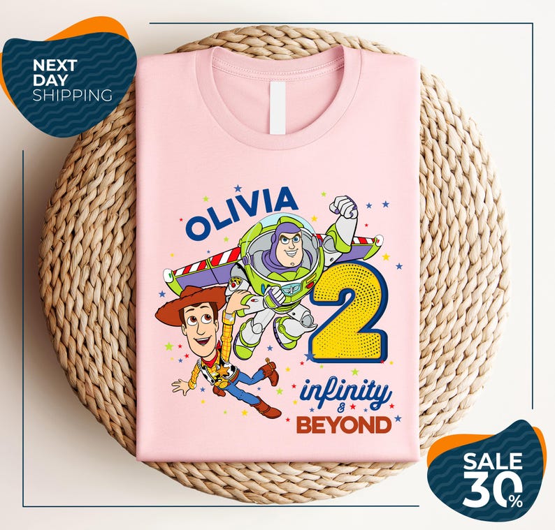 A pink t-shirt with a cartoon image of Buzz Lightyear and Woody from Toy Story, along with the text "Olivia 2 Infinity Beyond".