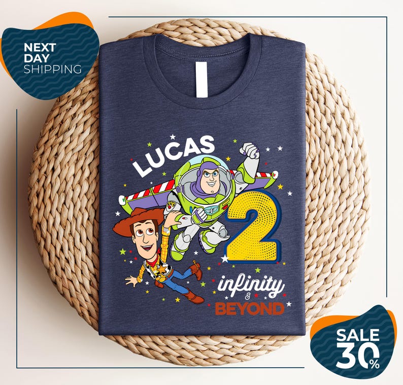 A blue t-shirt with a graphic design featuring characters from the Toy Story franchise, specifically Buzz Lightyear and Woody, along with the text "Lucas 2" and " Infinity & Beyond".