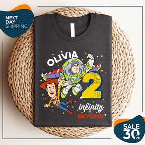 A gray t-shirt with a graphic design featuring characters from the Toy Story franchise, specifically Buzz Lightyear and Woody, along with the text "Olivia 2 infinity & beyond".