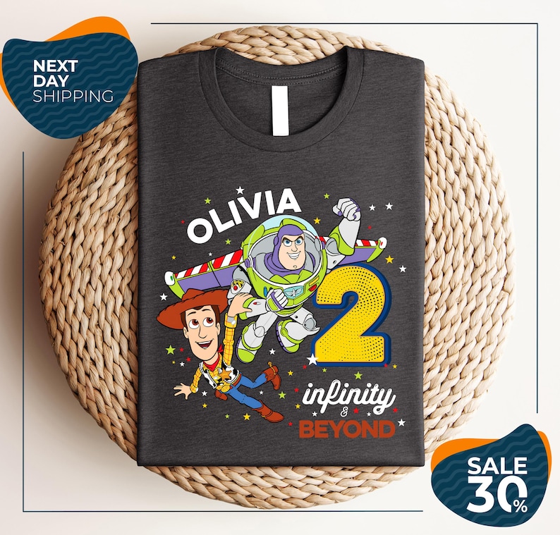 A gray t-shirt with a graphic design featuring characters from the Toy Story franchise, specifically Buzz Lightyear and Woody, along with the text "Olivia 2 infinity & beyond".