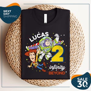A black t-shirt with a colorful graphic design featuring characters from the Toy Story franchise, including Buzz Lightyear and Woody, along with the text "Lucas 2 infinity & beyond".