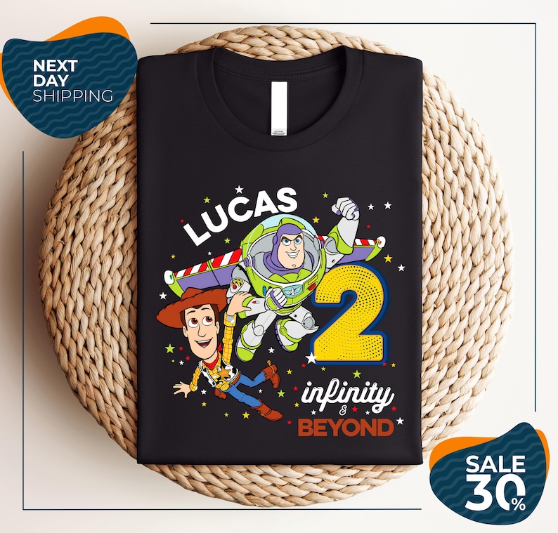 A black t-shirt with a colorful graphic design featuring characters from the Toy Story franchise, including Buzz Lightyear and Woody, along with the text "Lucas 2 infinity & beyond".