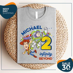 A gray t-shirt with a graphic design featuring characters from the Toy Story franchise, including Buzz Lightyear and Woody, along with the text "Michael 2 Infinity & Beyond".