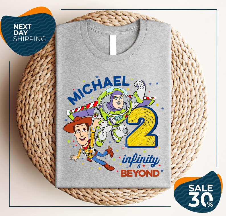 A gray t-shirt with a graphic design featuring characters from the Toy Story franchise, including Buzz Lightyear and Woody, along with the text "Michael 2 Infinity & Beyond".