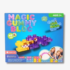 Könnte beinhalten: Eine Schachtel mit Magic Gummy Bloc Bausteinen mit 40 Teilen. Die Verpackung zeigt eine aus violetten und gelben, durchscheinenden und weichen Blöcken gebaute Kreatur sowie den Text 'Magic Gummy Bloc', 'Ages 3+' und 'Super Soft'.