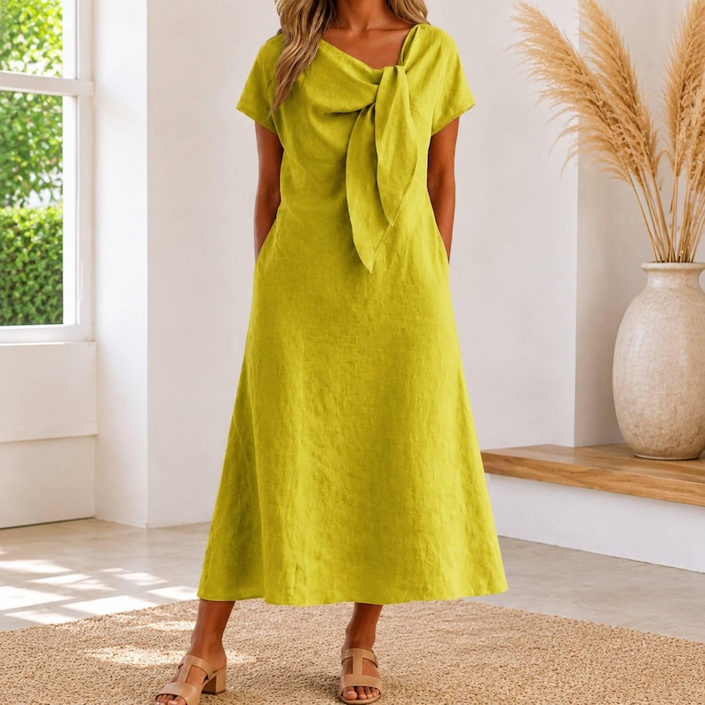 May include: A lime green midi dress featuring short sleeves, a round neckline, and a prominent fabric tie detail centered at the chest. The dress has a relaxed, A-line silhouette that falls to the mid-calf, providing a simple and clean aesthetic.